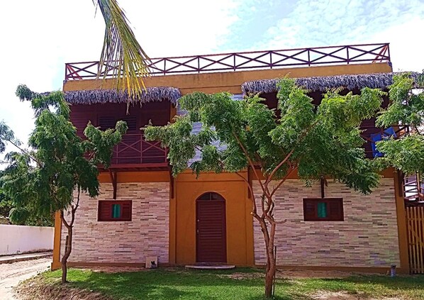 A building with a thatched roof, a central arched entrance, and a stone facade. - Residencial Bem Te Vi (Jijoca de Jericoacoara)