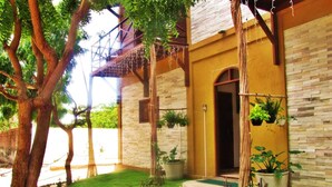 A house with a wooden deck, a brick exterior, and a small garden with a pathway leading to the door. - Residencial Bem Te Vi (Jijoca de Jericoacoara)