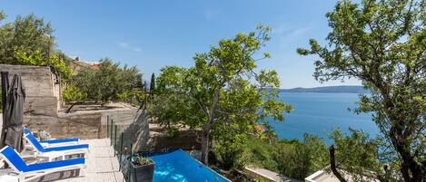 A swimming pool with blue lounge chairs, a ladder, and a view of the sea.