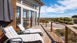 A deck with lounge chairs and a wooden railing overlooking a road and greenery. - Lakeview - A modern and beautifully designed holiday home (Marion Bay)