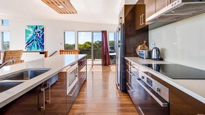 A modern kitchen with a central island, stainless steel appliances, and a view to a balcony. - Lakeview - A modern and beautifully designed holiday home (Marion Bay)