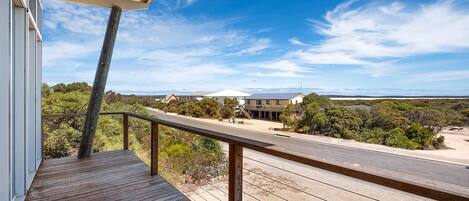 A wooden deck with a railing overlooking a road and houses in a coastal area.