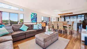 A modern living room with a brown sofa, a coffee table, and a dining area with wicker chairs. - Lakeview - A modern and beautifully designed holiday home (Marion Bay)