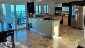 Una cocina moderna con una isla central, electrodomésticos de acero inoxidable y vista al océano.
