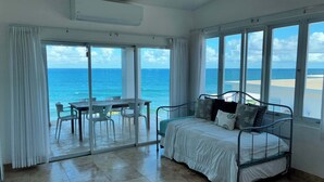 Una habitación con cama, una mesa, sillas y vistas a la playa y al océano.