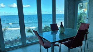 Una habitación con una mesa y sillas de vidrio, un jarrón y vista al océano.