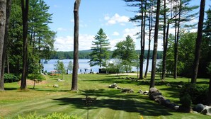 Un campo de golf bien cuidado con vista a un lago, rodeado de altos árboles y un cielo despejado.
