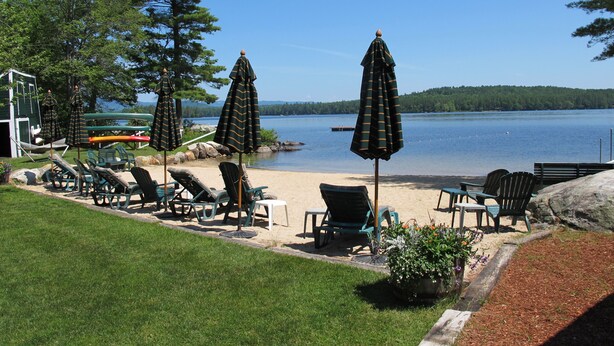 Un patio frente al lago con sillones de descanso, sombrillas y vistas al lago.