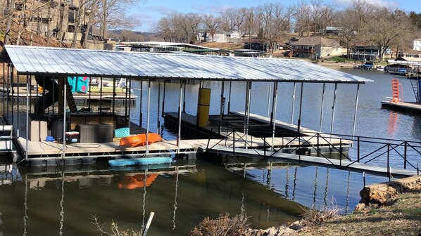 Un barco amarrado con zona de estar cubierta, una lancha pequeña y un cuerpo de agua con reflejos.