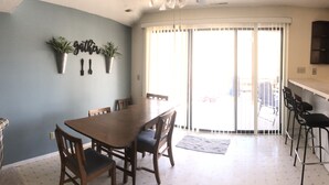 A dining area with a wooden table and chairs, a potted plant, and a wall-mounted sign.