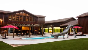 Un espace piscine avec un toboggan, des sièges extérieurs et un bâtiment doté de grandes fenêtres.