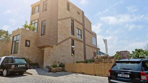 A modern building with a stone facade, a flag, and two parked cars. - Batroun Bahsa Bay (Batroun)