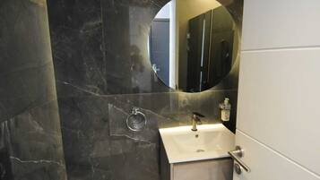 A bathroom with a marble wall, a sink with a mirror, and a door.