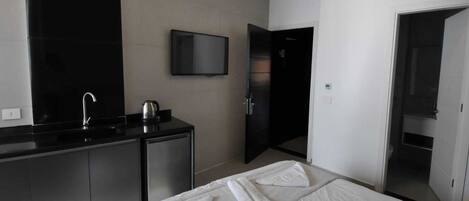 Habitación de hotel moderna con una cama, un televisor de pantalla plana en la pared, una pequeña kitchenette y un baño visible a través de una puerta abierta.