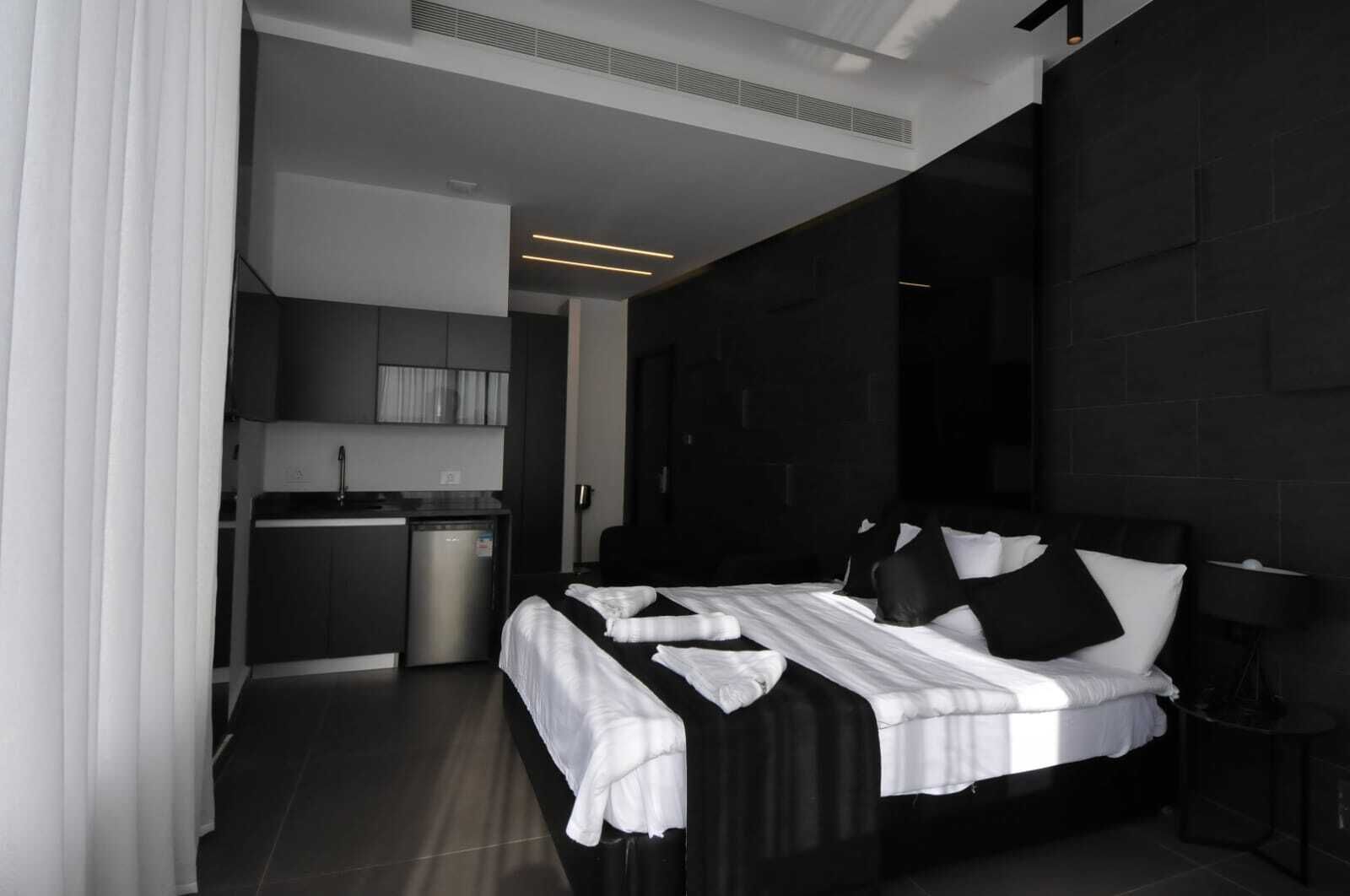 Une chambre d’hôtel moderne dotée d’un grand lit, d’une kitchenette séparée et d’un mur d’accent de couleur sombre.