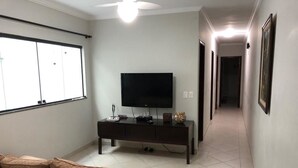 Una sala de estar con un televisor de pantalla plana sobre un mueble de madera oscura, un sofá marrón y un pasillo con cuadros enmarcados en las paredes.