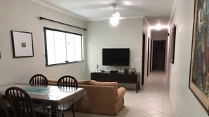 Un comedor con mesa y sillas, un sofá, un televisor y un pasillo con un cuadro.