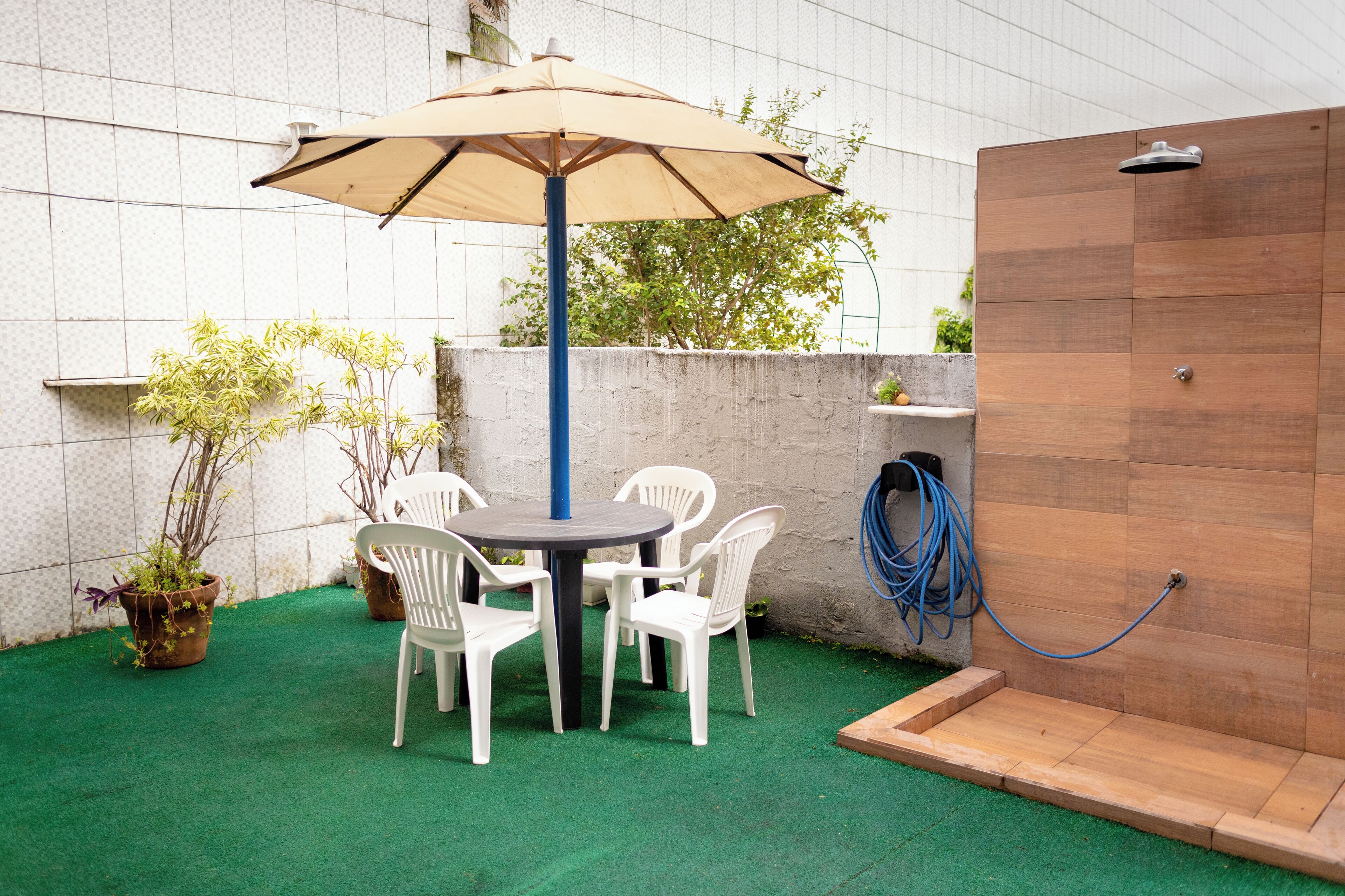 A patio with a round table and four white chairs, an umbrella, and a wooden shower enclosure.