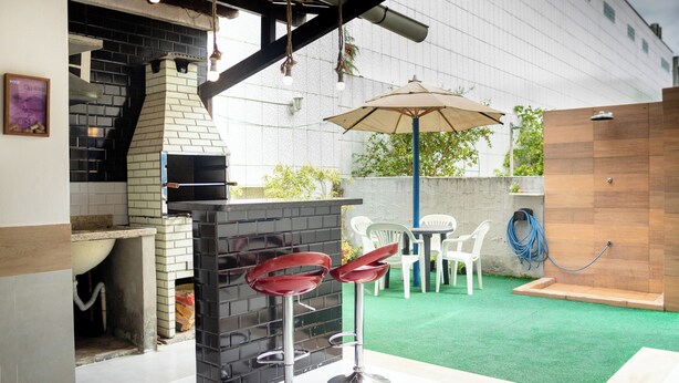 Un patio al aire libre con una chimenea de ladrillo, dos taburetes rojos, una mesa con sillas y césped artificial verde.