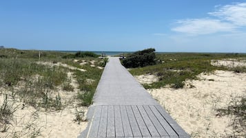 Une promenade en bois menant à la plage, entourée de dunes de sable et d’une végétation clairsemée.