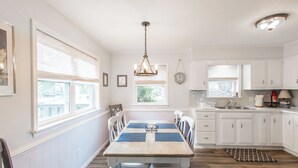 Una cocina con armarios blancos, una mesa de comedor de madera y una lámpara colgante.