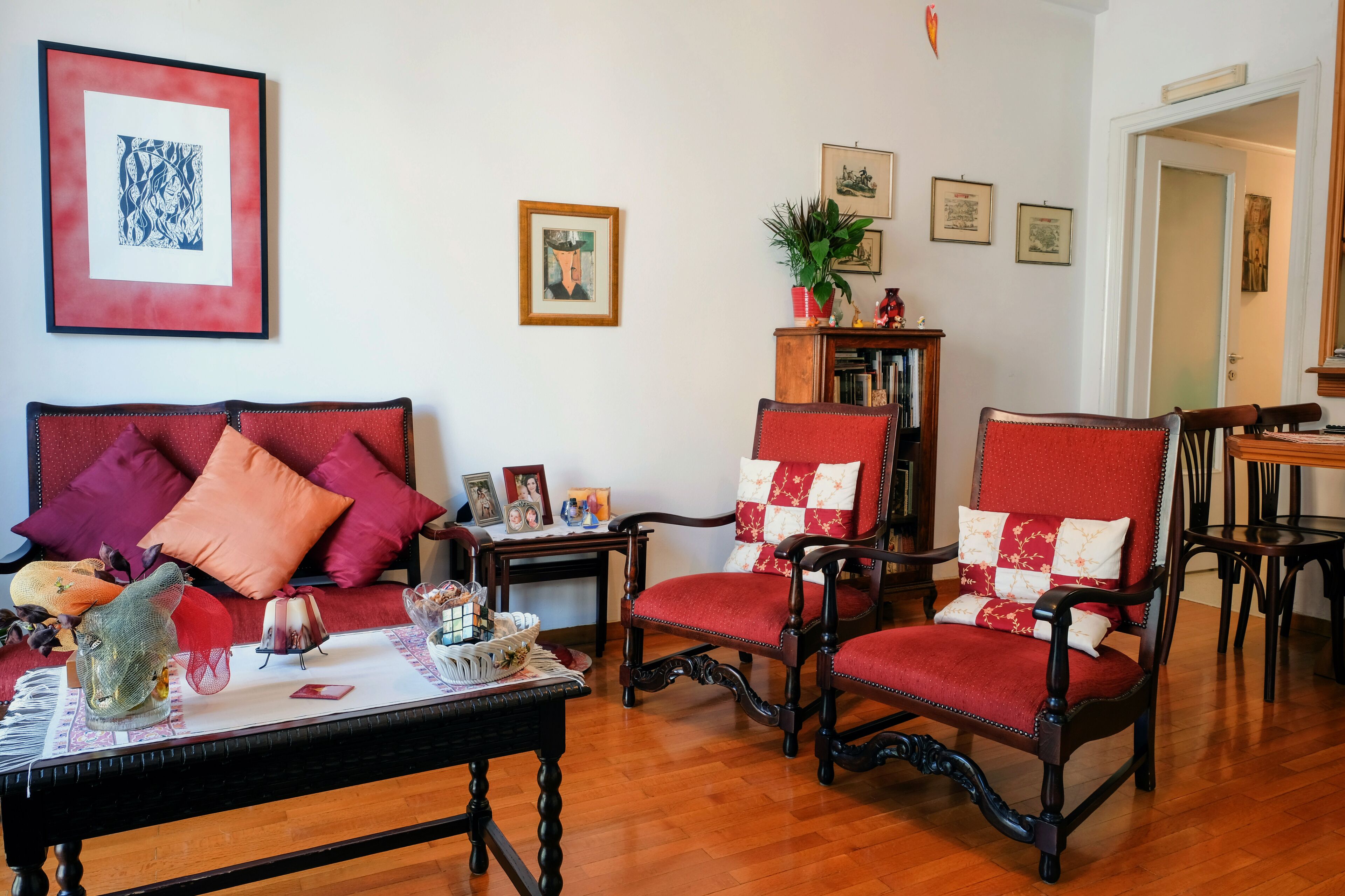 Una sala de estar con un sofá rojo, dos sillones rojos, una mesa de centro de madera y una estantería.