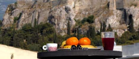 A table with fruits, a cup, and a glass of red drink, overlooking ancient ruins.
