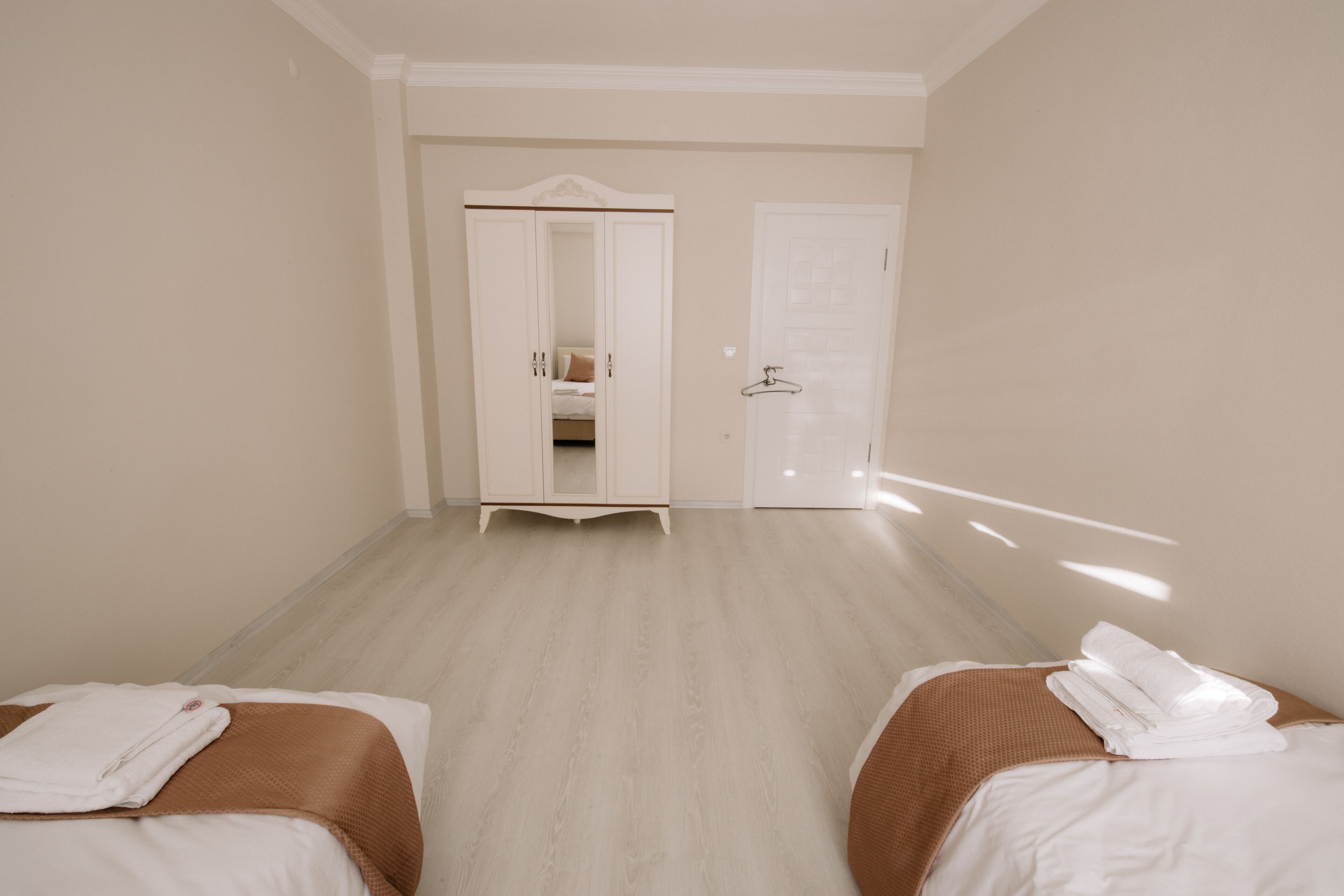 A hotel room with two beds, a wardrobe, and a door leading to a bathroom.