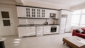 Eine moderne Küche mit weißen Schränken, einer Granit-Arbeitsplatte und einem eingebauten Ofen. Im Wohnbereich befindet sich eine rote Couch und ein Holztisch.