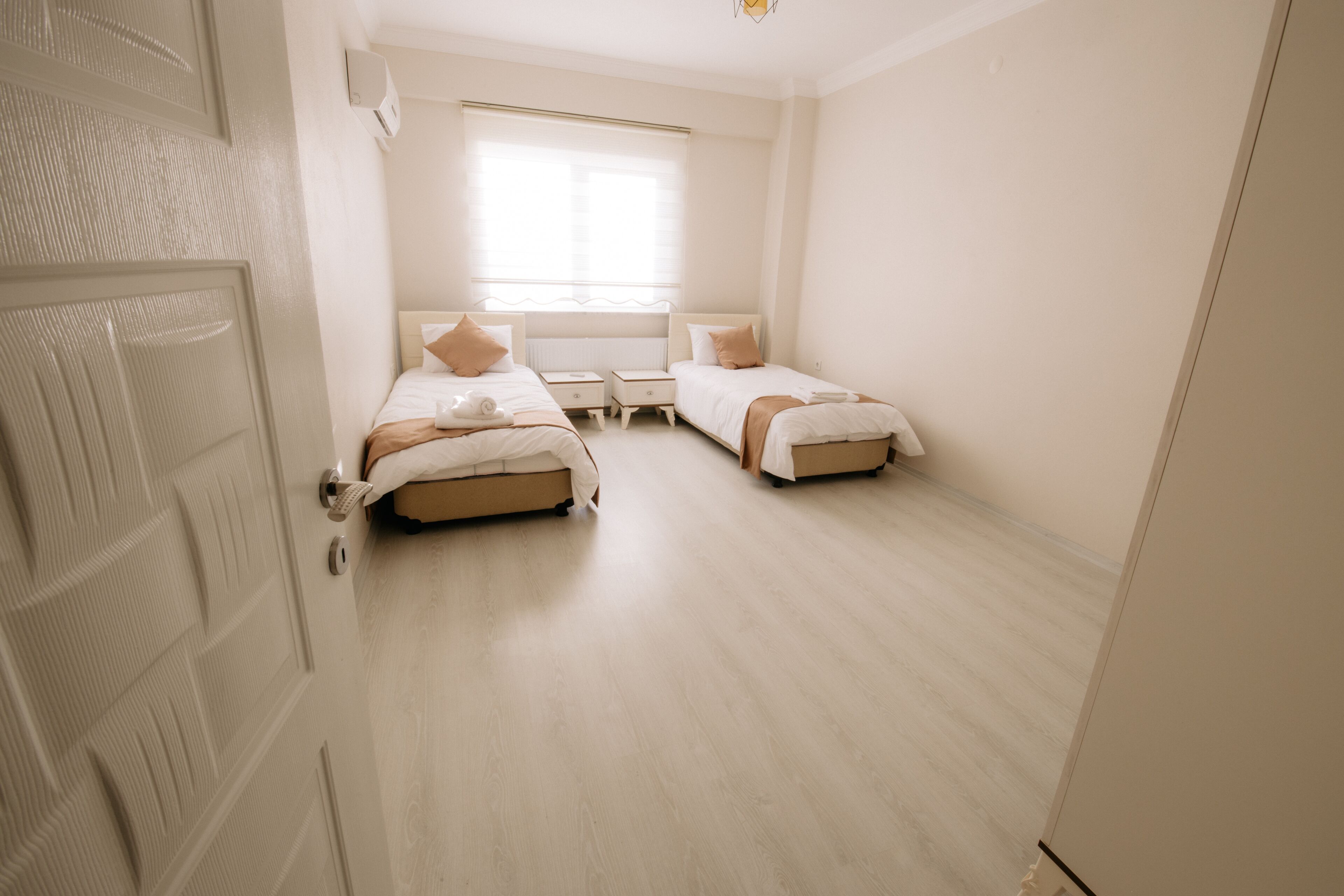 A bedroom with two beds, a window, and a door.