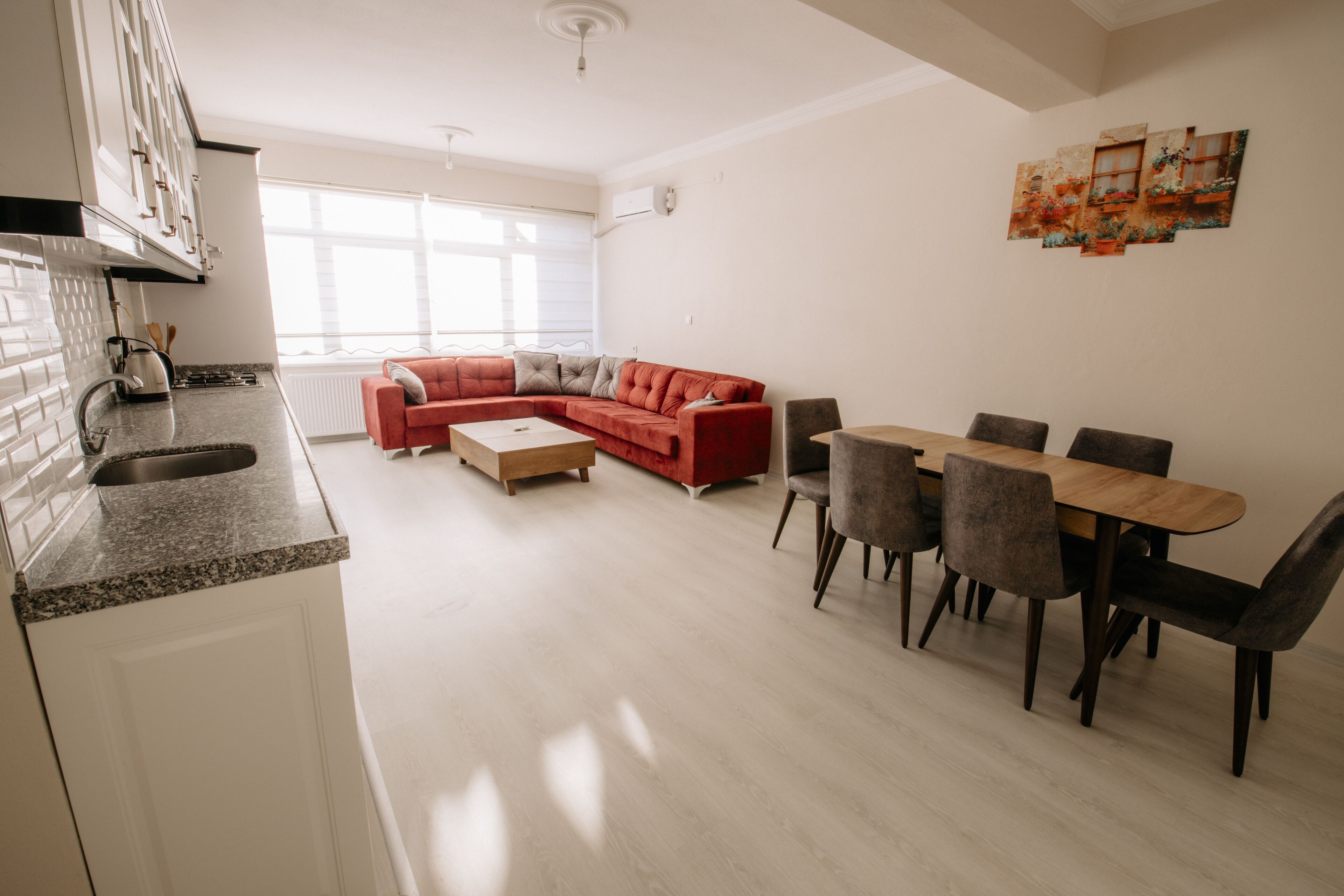Una cocina moderna con armarios blancos y encimera de granito. En la sala de estar, hay un sofá seccional rojo y una mesa de comedor con sillas.