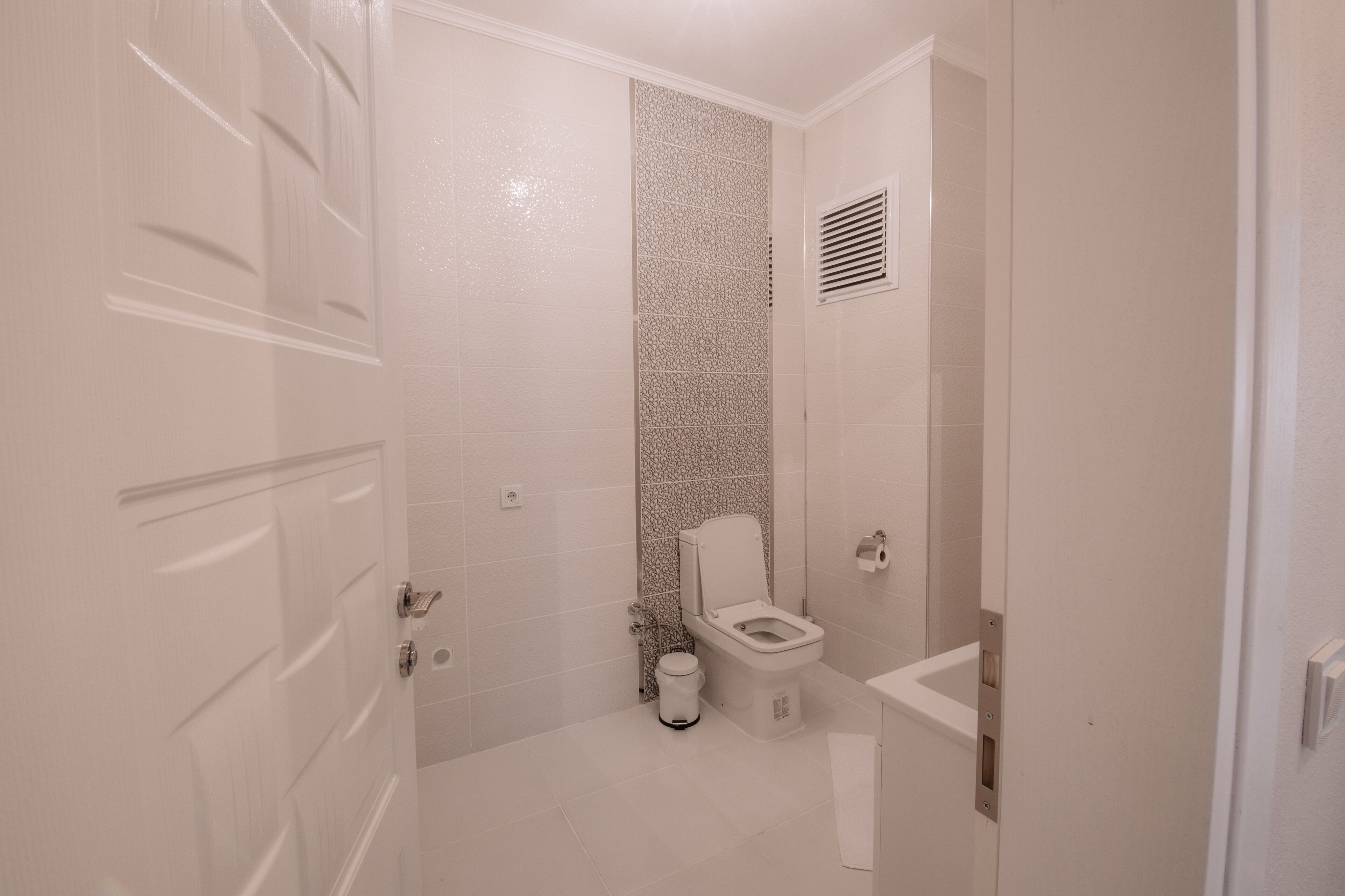 Ein kleines, weißes Badezimmer mit Toilette, Mülleimer und Duschbereich.