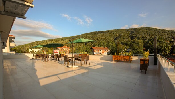 Eine Terrasse im Freien mit Tischen, Stühlen, Sonnenschirmen und Blick auf einen bewaldeten Hügel.