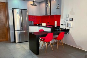 Une cuisine moderne avec un réfrigérateur en acier inoxydable, un mur d’accent rouge et deux chaises rouges disposées autour d’un îlot central noir.