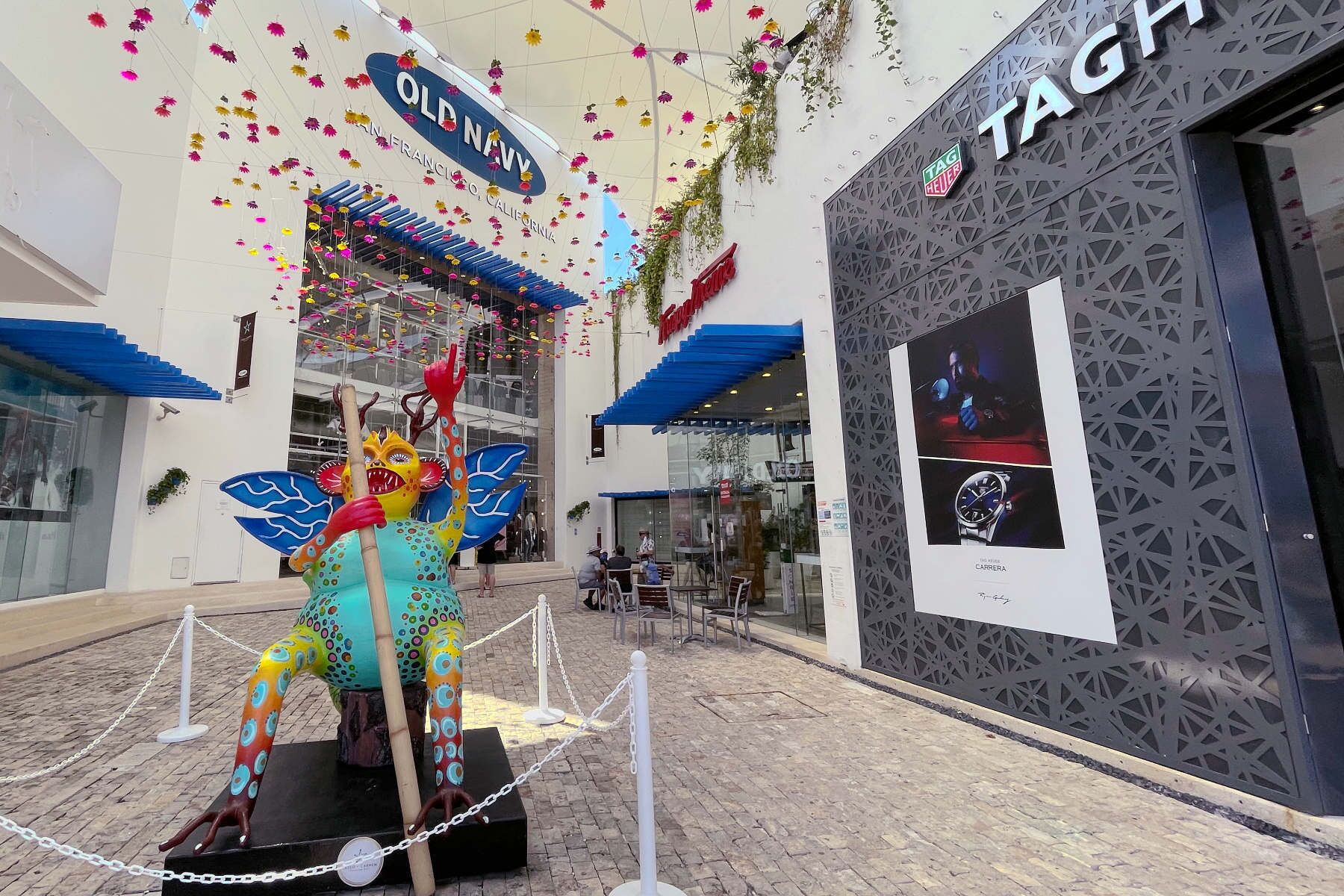 A shopping mall with a colorful sculpture of a sea creature in front of a TAG Heuer store.