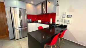 Une cuisine moderne avec des appareils en acier inoxydable, un plan de travail noir et des chaises rouges.