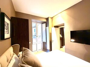 Una habitación de hotel con cama, televisor, puerta que da a un balcón y un cuadro colgado en la pared.