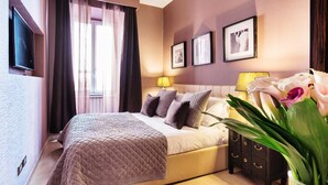 Un dormitorio con cama, mesita de noche, lámpara, televisor y cuadros en la pared.
