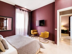 Une chambre d’hôtel avec un lit, deux fauteuils jaunes, un téléviseur fixé au mur et une grande fenêtre avec des rideaux.