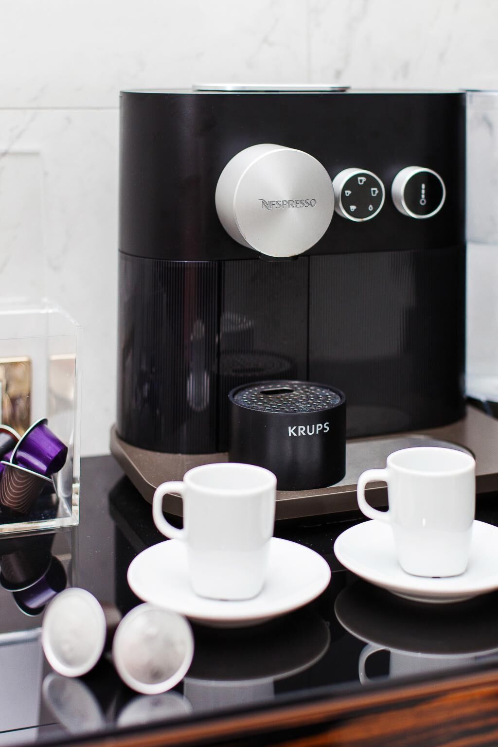 A coffee machine with a Krups brand coffee pot, two white cups, and a glass container with purple lids.