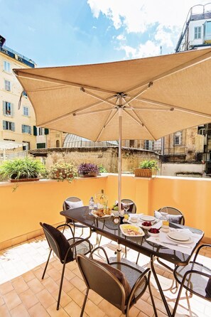 Une terrasse extérieure avec une table dressée pour le repas, entourée de chaises et protégée par un grand parasol.