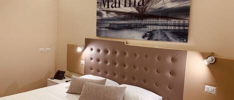 A hotel room with a large bed, a headboard with a tufted design, two bedside lamps, and a framed picture of a bridge on the wall.