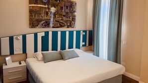 Una cama bien hecha con cabecera a rayas, una mesita de noche con lámpara y una obra de arte en la pared que representa un paisaje urbano.