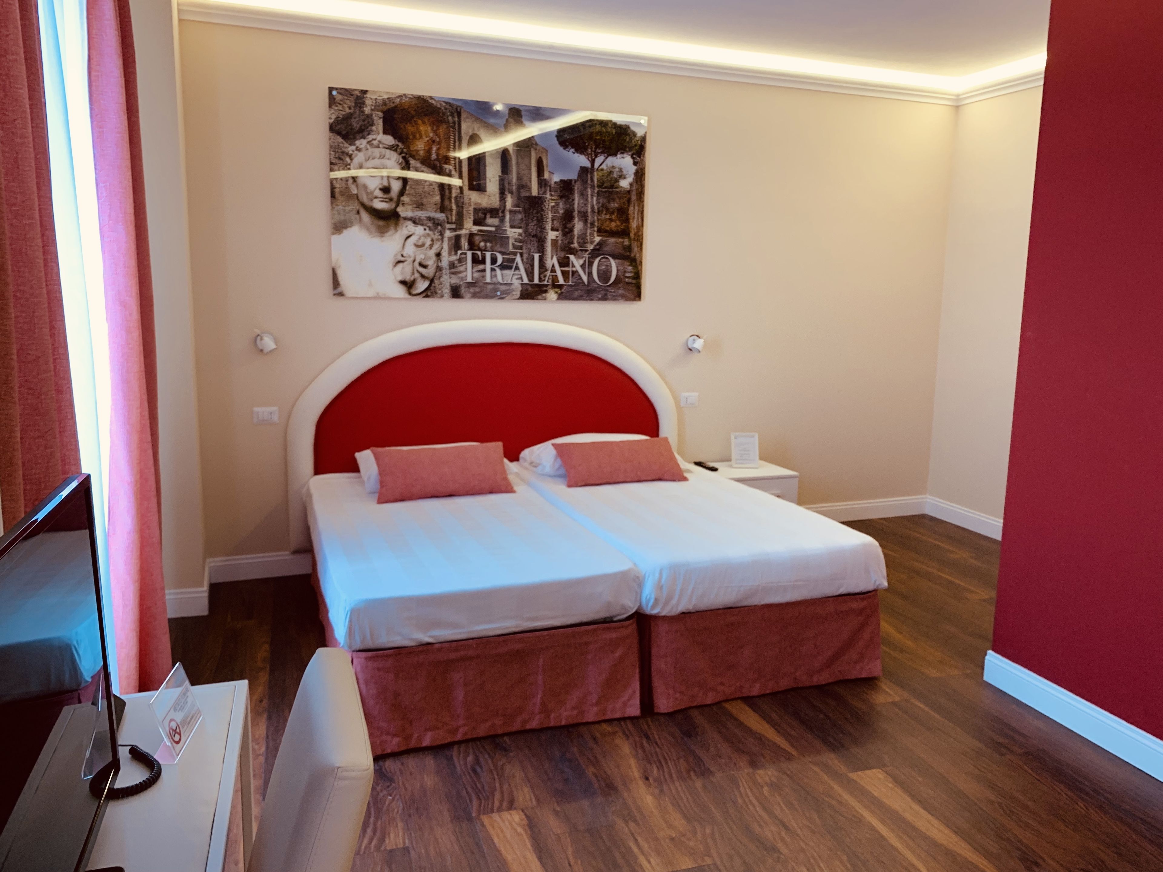 A double bed with a red headboard, two pillows, and a nightstand with a lamp.