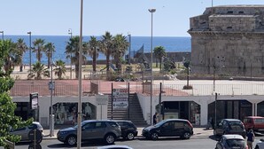 Una calle costera con coches aparcados, palmeras y un edificio histórico.