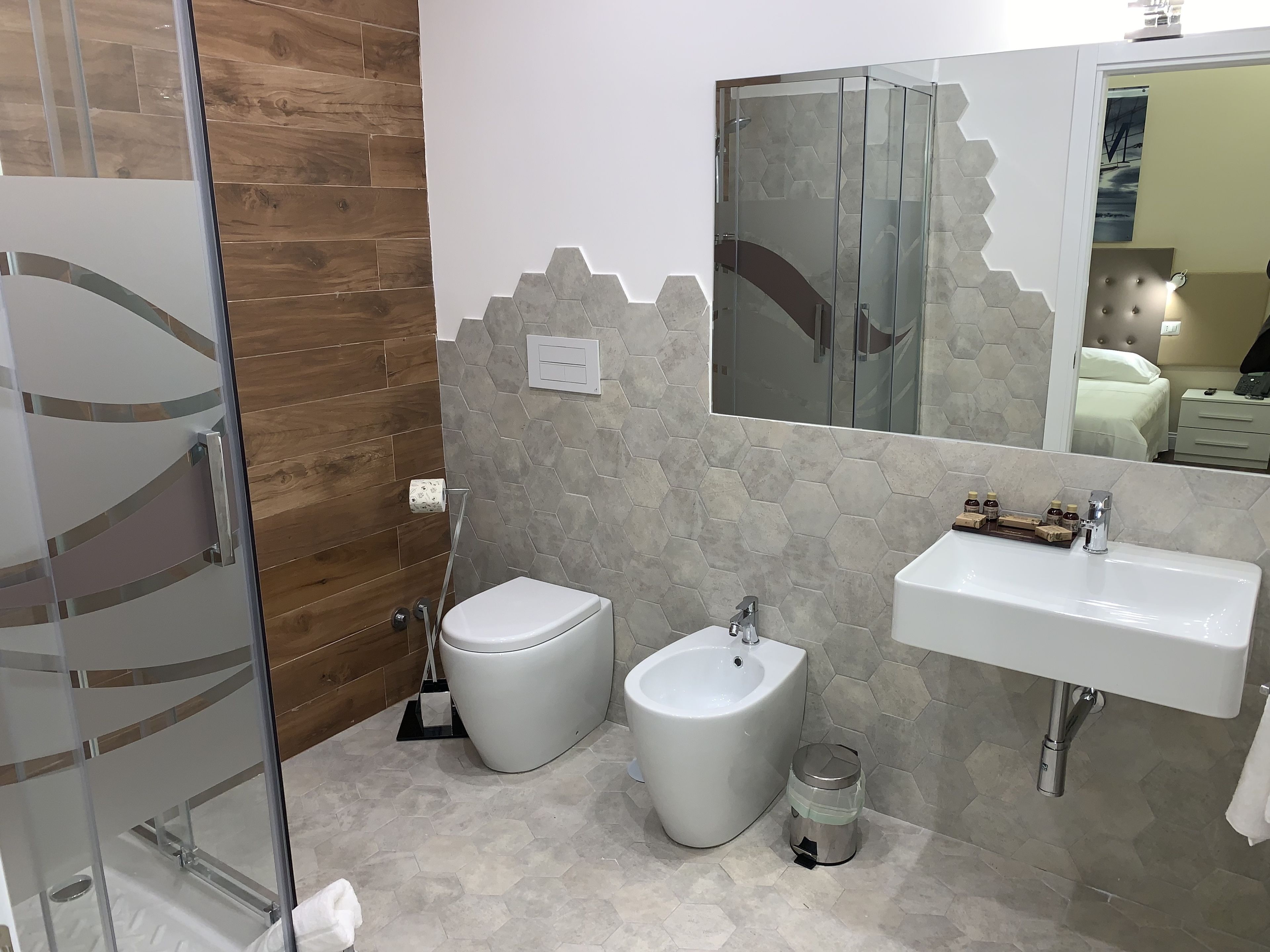 Une salle de bain équipée de toilettes, d’un bidet et d’un lavabo, avec un mur en bois et un revêtement de sol en carrelage hexagonal.