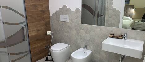 A bathroom with a toilet, bidet, and sink, featuring a wooden wall and hexagonal tile flooring.