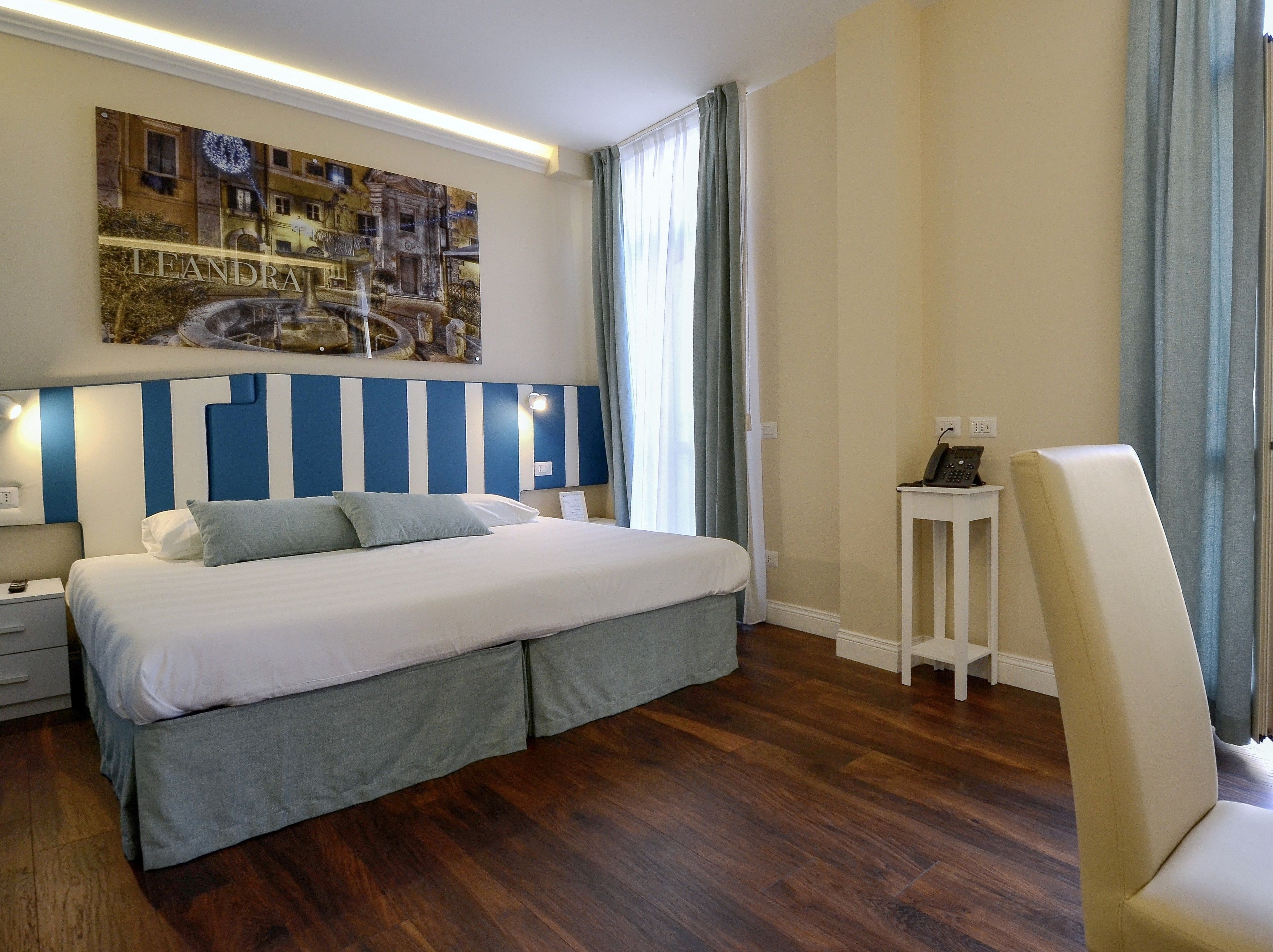 Quarto de hotel com uma cama grande, uma mesa de cabeceira, uma pequena mesa com um telefone e uma cadeira.