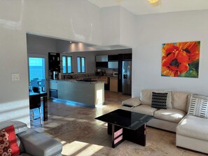 A modern living room with a sofa, a glass coffee table, and a view of the kitchen and dining area.