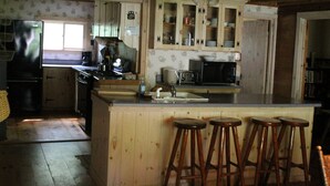 Una cocina con armarios de madera, un refrigerador, un lavamanos y taburetes de bar.